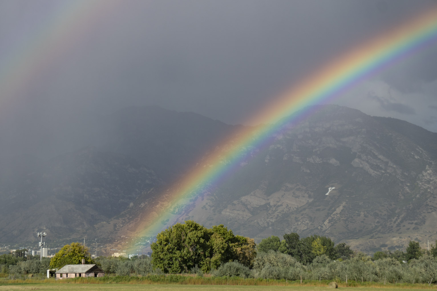 A bright rainbow rises to the right not far over the letter Y on the mountainside